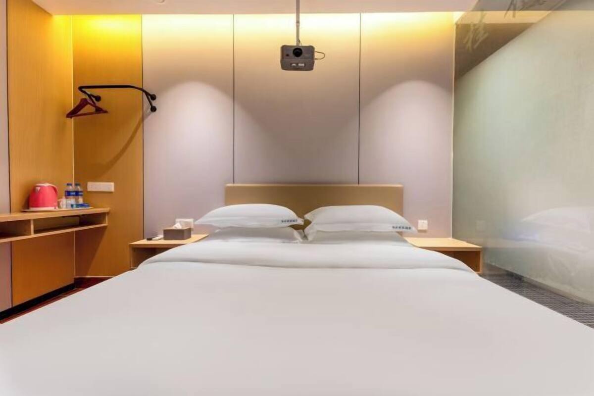 A hotel room with a bed, bedside tables, a projector, and a wardrobe.