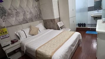 Quarto de hotel com cama, mesa de cabeceira, guarda-roupa, banheiro com pia e espelho, e um tapete azul no chão.