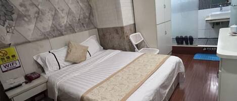 Une chambre d’hôtel comprenant un lit, une table de chevet, une armoire, une salle de bain avec un lavabo et un miroir, et un tapis bleu sur le sol.