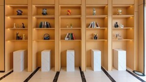 Ein modernes Interieur mit einer Reihe aus Holzböden und Marmorsockeln, auf denen verschiedene Dekorationsobjekte und Bücher präsentiert werden.
