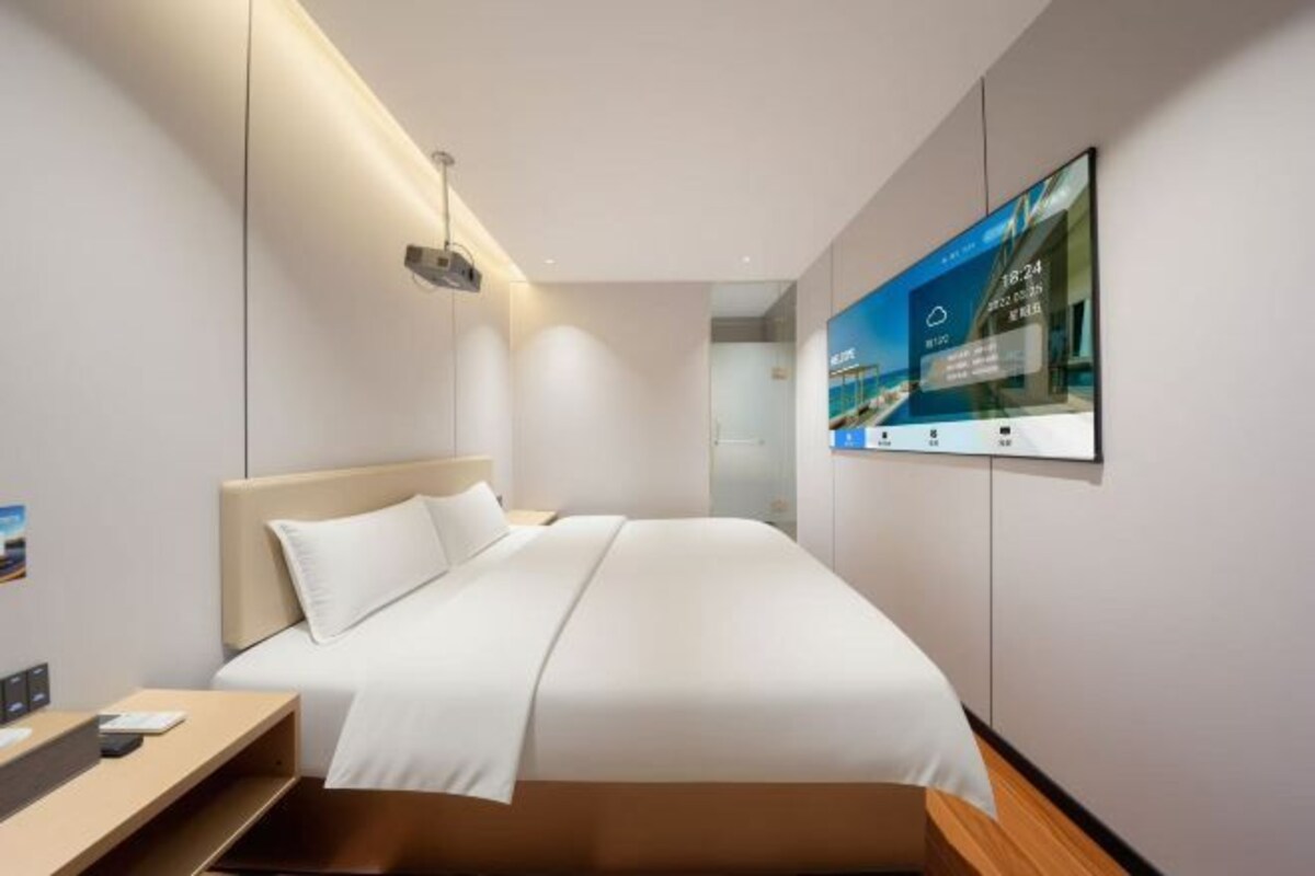 A modern hotel room with a bed, bedside table, and a mounted TV displaying a cityscape.