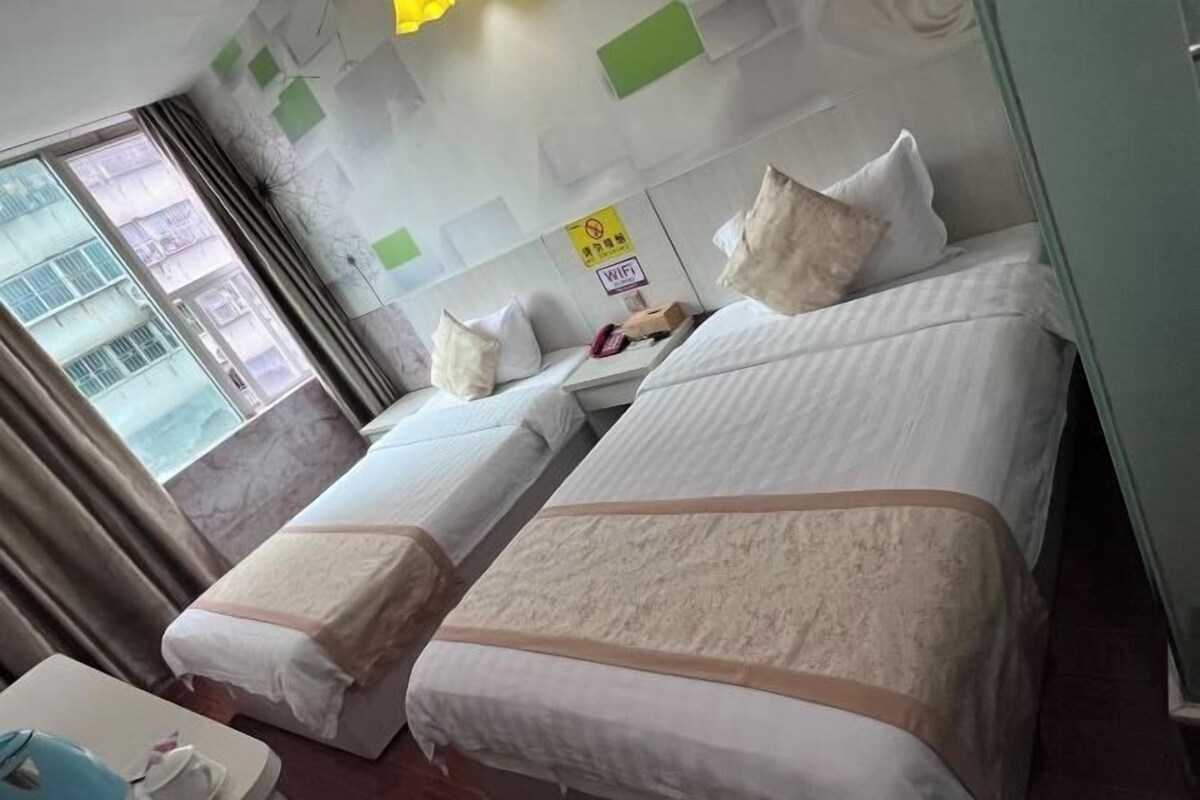 A hotel room with two beds, a desk, and a window.