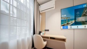 Ein Hotelzimmer mit Schreibtisch, Stuhl, Fernseher, Klimaanlage und einem Fenster mit Vorhängen.