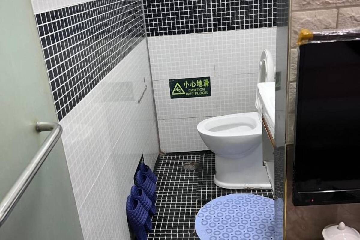 A bathroom with a wet floor sign, a toilet, a sink, and a shower area.
