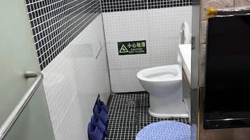 Casa de banho com aviso de chão molhado, sanita, lavatório e zona de duche.