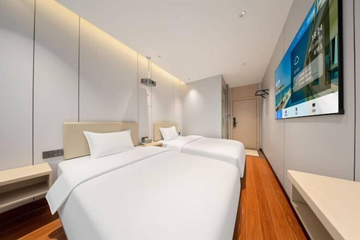A hotel room with two beds, a large mirror, a flat-screen TV, and a wooden floor.