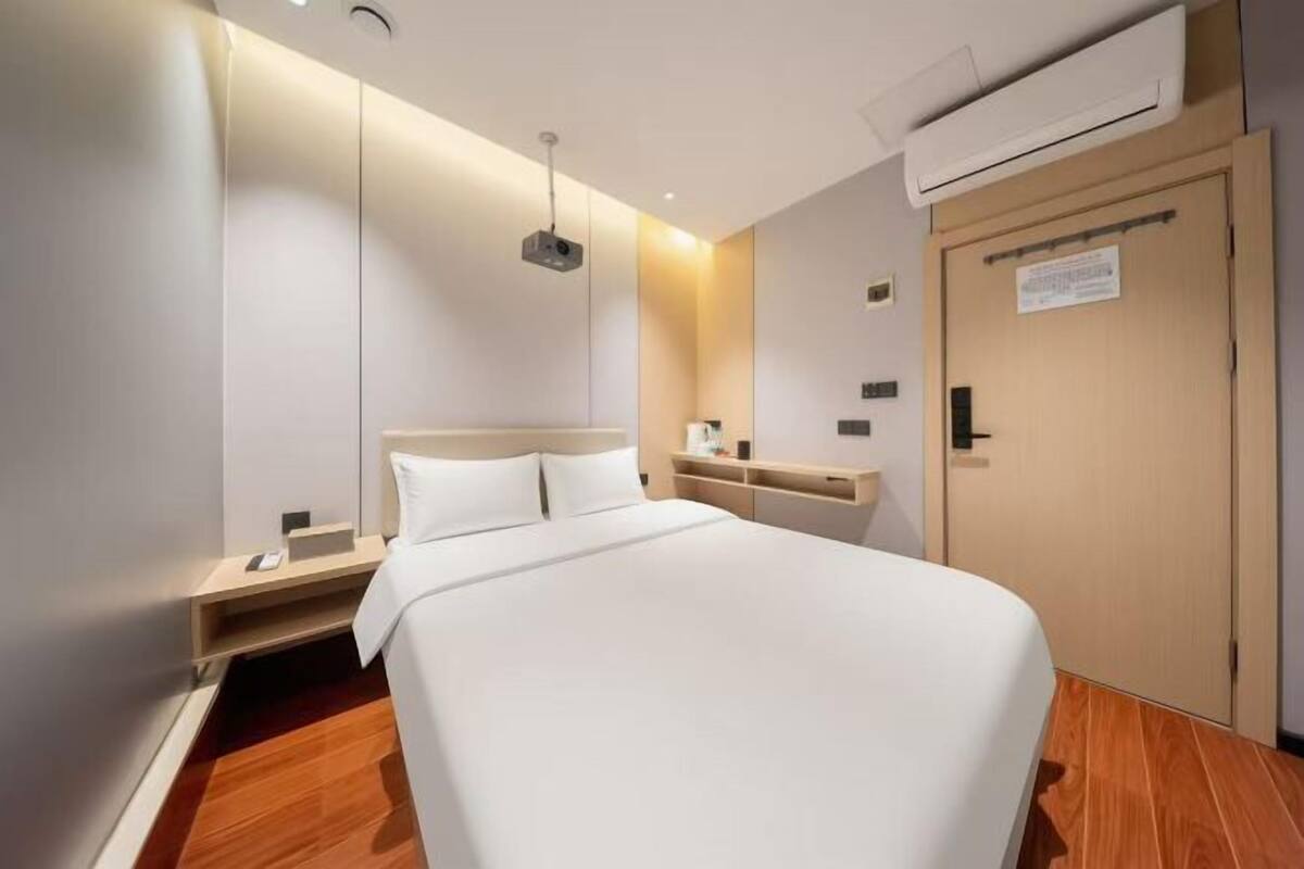 A modern hotel room with a large bed, bedside tables, a wardrobe, and an air conditioning unit.