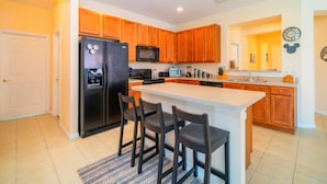 Una cocina moderna con armarios de madera, un refrigerador negro, un microondas y una isla grande con taburetes de bar.
