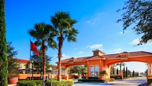 Entrada de hotel con una bandera roja, palmeras y un edificio anaranjado.