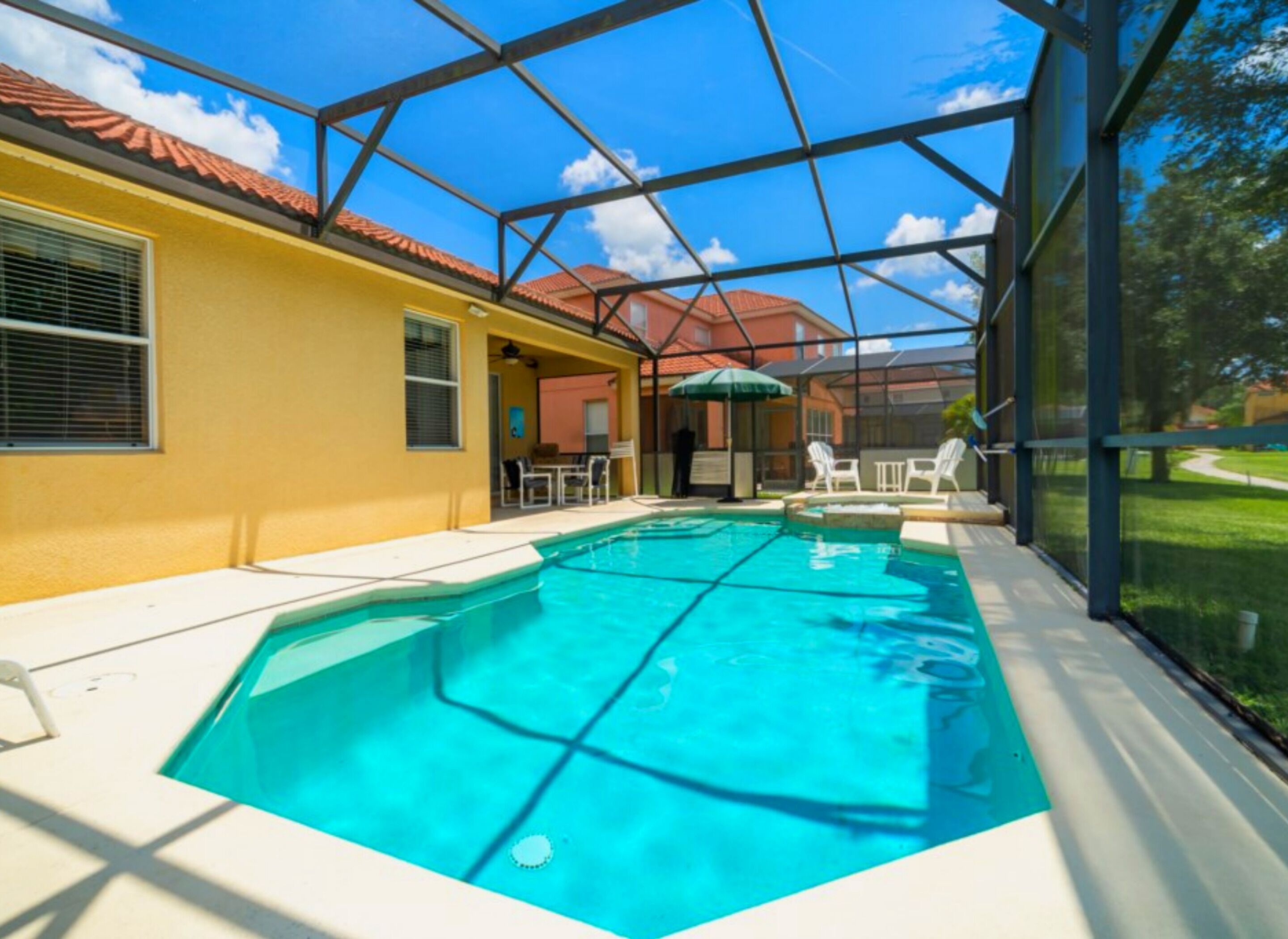 A swimming pool with a glass enclosure, surrounded by a patio area with chairs and a table.