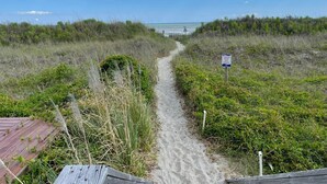 Een zandpad dat naar een strand leidt, met een bordje dat waarschuwt om van de duinen af te blijven.