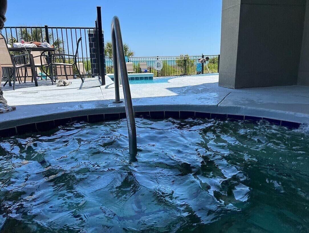 A swimming pool with a metal ladder, a tiled deck, and a view of the surrounding area.