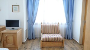 A room with a wooden cabinet, a television on top, a striped chair, and a window with blue curtains. - Hotel Sternen (Aarau)