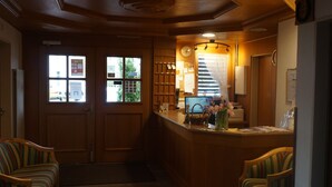 A reception area with a wooden counter, a clock, and a window with a view of the outside. - Hotel Sternen (Aarau)