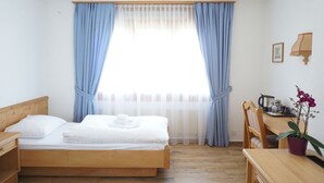 A bedroom with a wooden bed, a desk with a chair, a potted orchid, and a window with blue curtains. - Hotel Sternen (Aarau)