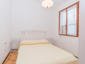 A small, single-bed room with a wooden headboard, a window with curtains, and a ceiling light.