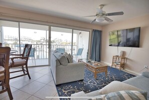 A spacious living area with a balcony, a ceiling fan, a flat-screen TV, and a dining table with chairs. - Comfortable Condo w/marina and ICW views & Private Beach Access (Placida)