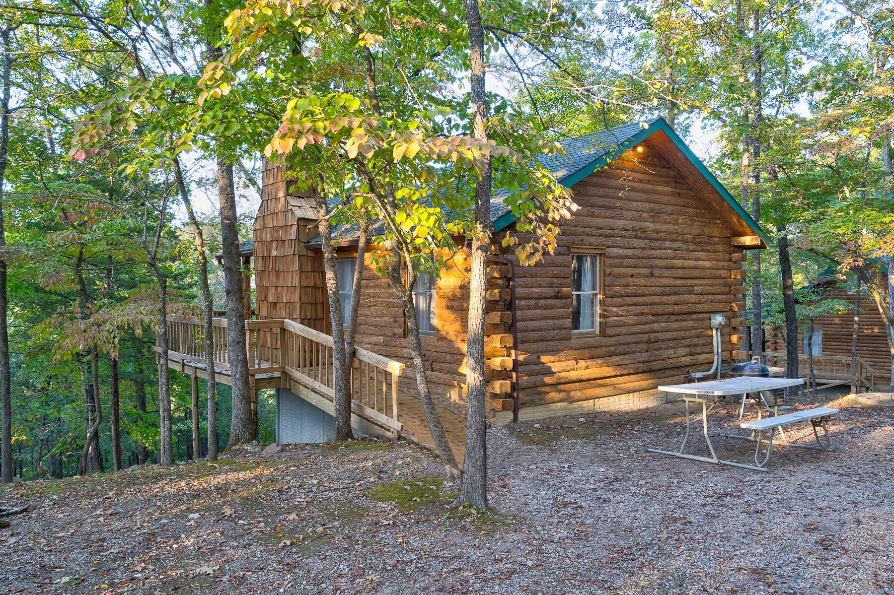 Una cabaña de troncos con un porche y una mesa de picnic en un área boscosa.