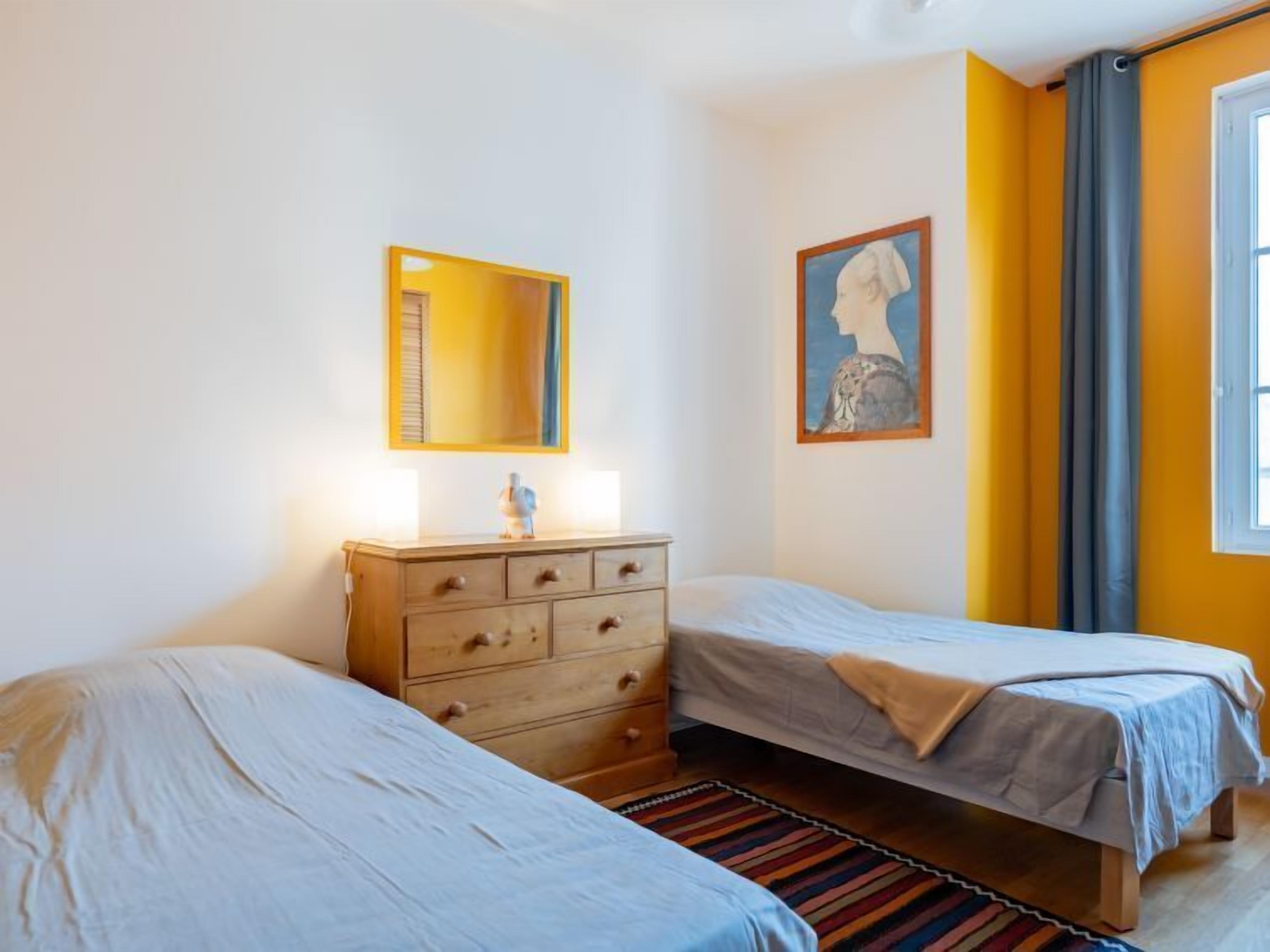 A room with two beds, a dresser, a mirror, and a painting.