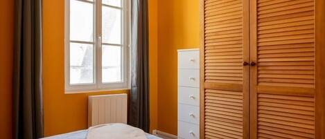A bedroom with a bed, a radiator, a window with curtains, and a wooden wardrobe.