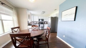 Un comedor con una mesa redonda y sillas, una cocina al fondo y una pared azul con un cuadro enmarcado.