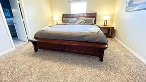 Un dormitorio con una cama grande, dos mesitas de noche, una ventana y una puerta que da a otra habitación.