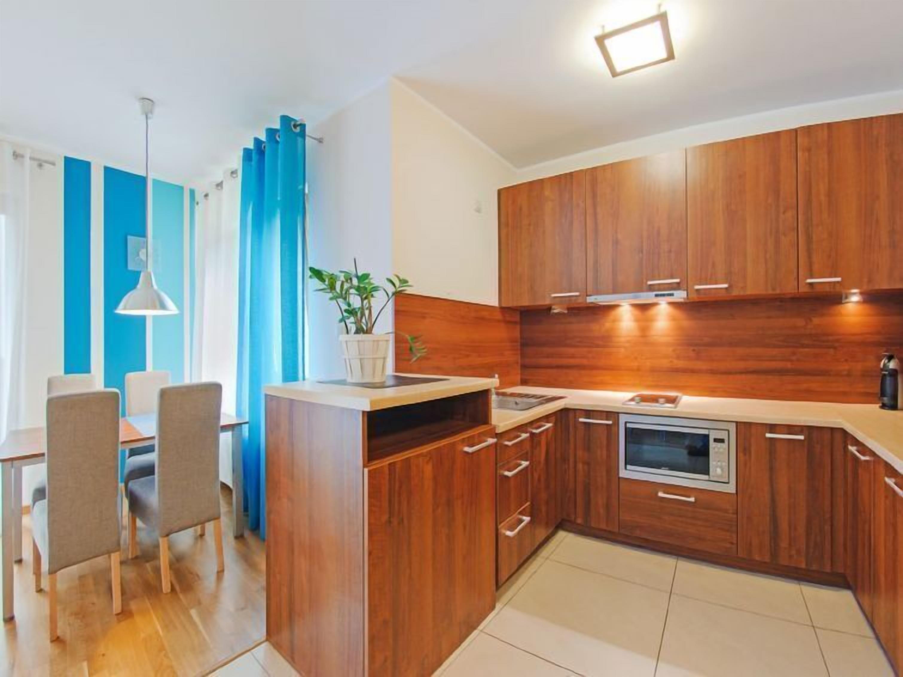 Eine moderne Küche mit Holzschränken, einer eingebauten Mikrowelle und einem Essbereich mit Tisch und Stühlen.