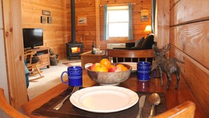 Un interior acogedor de cabaña con una mesa de comedor lista para dos, una chimenea y un televisor en la esquina.