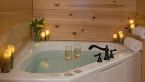 Una cabaña de madera con una bañera, velas y dos copas de vino.