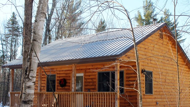 Una cabaña de madera con porche, rodeada de árboles y nieve.