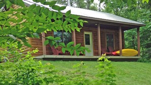 A wooden cabin with a porch, a red chair, and a yellow kayak. - Cozy Two Bedroom Cabin Near Smuggler's Notch (Jeffersonville)