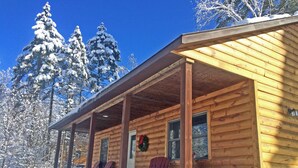 A wooden cabin with a porch, two Adirondack chairs, and a wreath on the door. - Cozy Two Bedroom Cabin Near Smuggler's Notch (Jeffersonville)