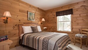 A wooden-paneled bedroom with a bed, two bedside lamps, a window, and a chair. - Cozy Two Bedroom Cabin Near Smuggler's Notch (Jeffersonville)