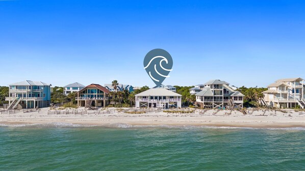 A beachfront property with multiple houses, a beach in the foreground, and a clear blue sky.