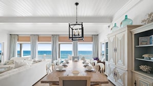 A dining area with a wooden table set for six, white chairs, and a view of the ocean. - OMG by the Sea: Beachfront in Plantation, Community Pool, One level (St. George Island)