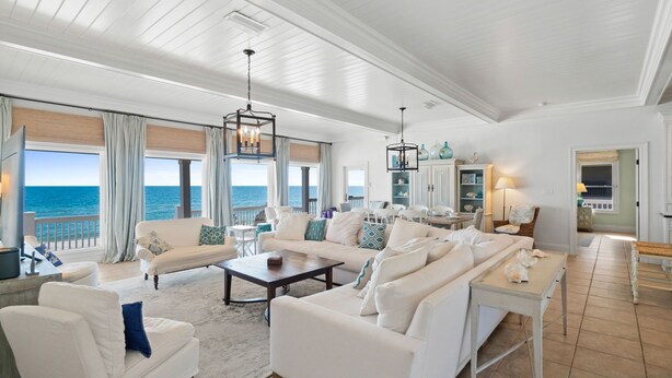 A spacious living room with white furniture, large windows overlooking the ocean, and a view of the sea. - OMG by the Sea: Beachfront in Plantation, Community Pool, One level (St. George Island)