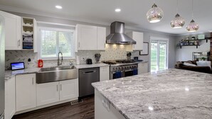 A modern kitchen with white cabinetry, a stainless steel range hood, and a marble countertop. - Spacious home with King bed - mins to Stadiums (Independence)