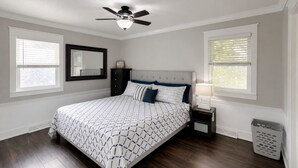 A bedroom with a bed, a ceiling fan, a nightstand, a lamp, a mirror, and a window. - Spacious home with King bed - mins to Stadiums (Independence)