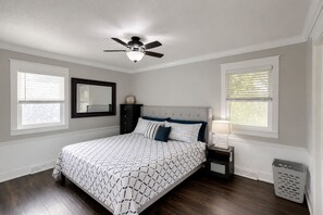 A bedroom with a bed, a ceiling fan, a nightstand, a lamp, a mirror, and a window.