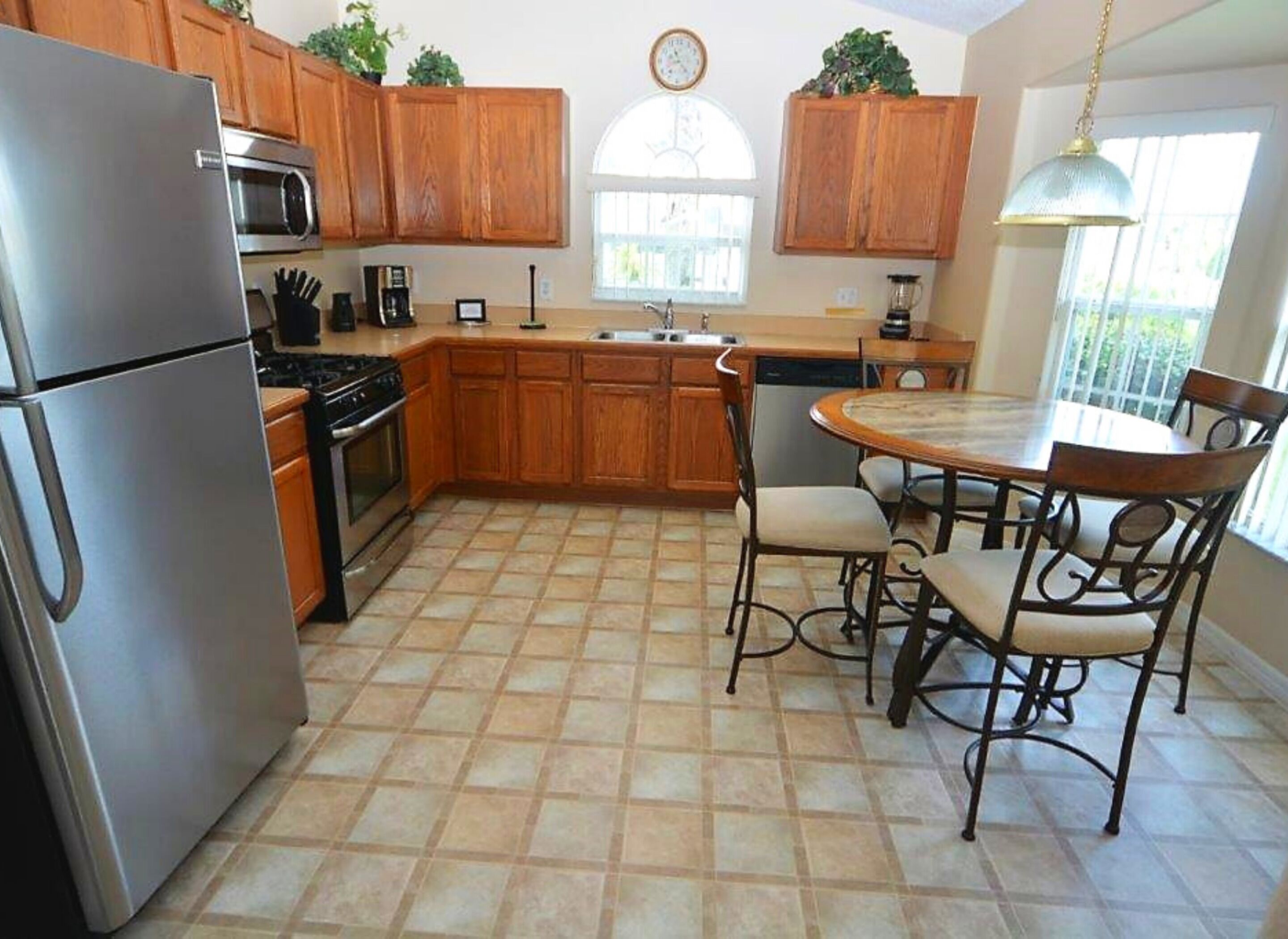 A kitchen with wooden cabinets, a stainless steel refrigerator, a stove, and a dining table with chairs.