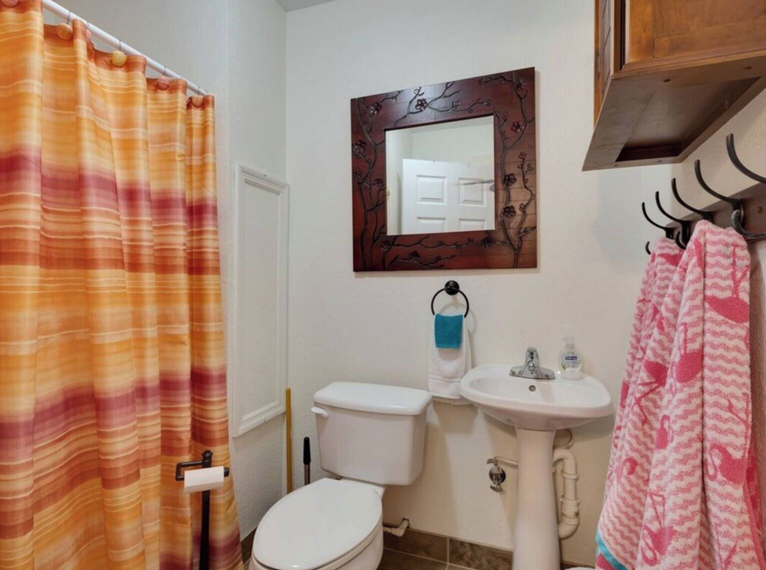 Une salle de bain avec un rideau de douche à rayures, des toilettes, un lavabo et un miroir orné d’un motif d’arbre.