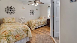 A bedroom with two beds, a ceiling fan, decorative wall art, and a wooden floor. - Cypress Cottage in the heart of Steinhatchee! Fenced in yard! (Steinhatchee)