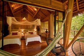 Una habitación de madera con dos camas, una hamaca y vistas al verdor exterior.