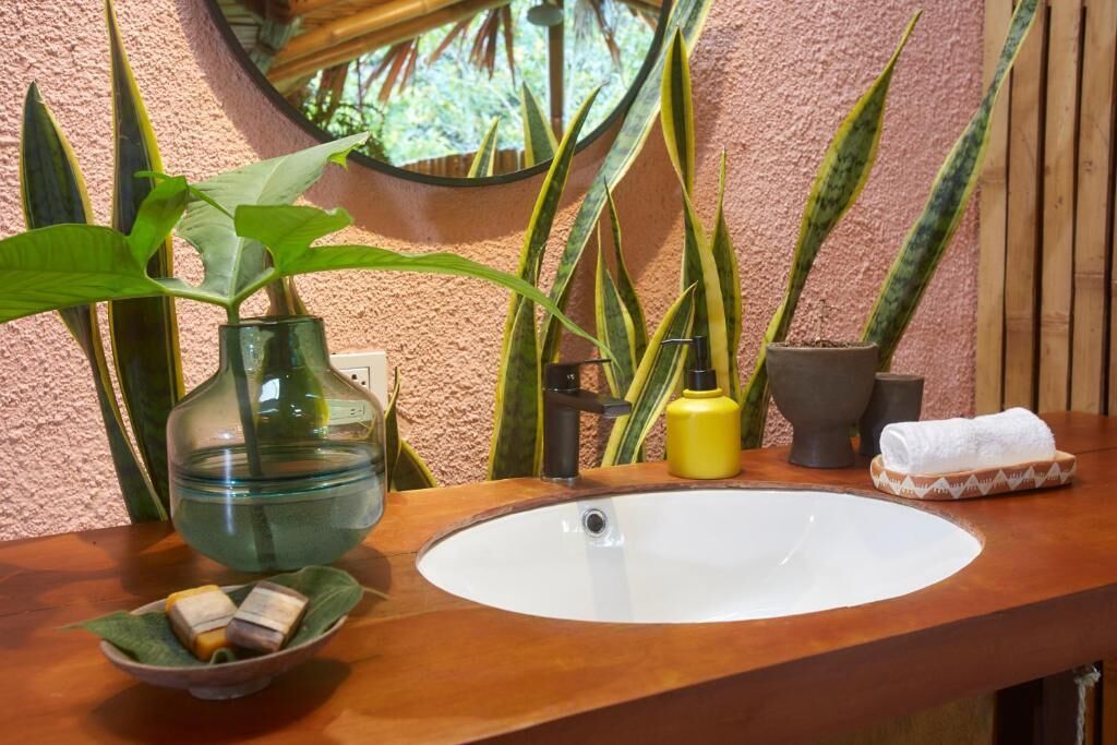 Un baño con tocador de madera, un lavabo blanco, un florero verde con una planta y un espejo.