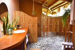 Un baño con tocador de madera, suelo de baldosas de piedra y cerramiento de bambú.