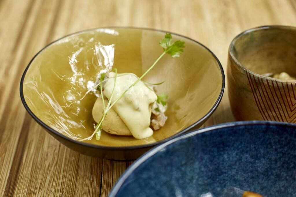 A bowl of food with a creamy sauce and garnish on a wooden table.