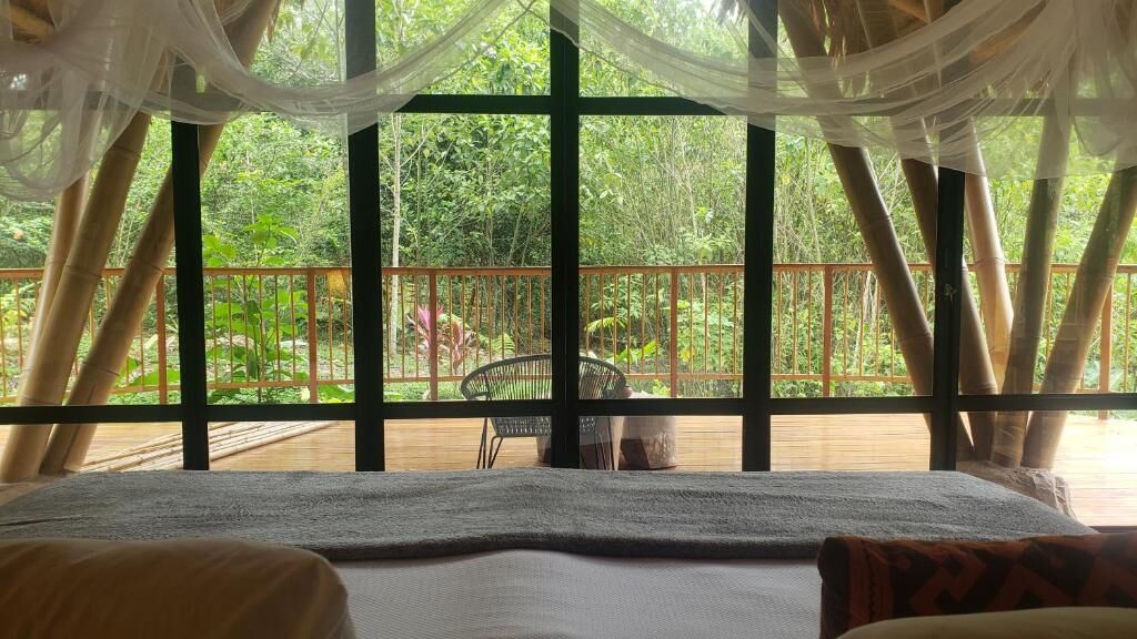 Quarto com uma janela grande e vista para uma varanda com uma cadeira e planta em vaso.