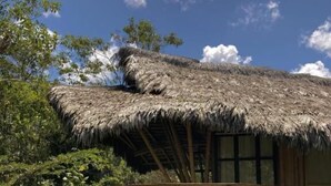 Uma construção com telhado de palha e deck de madeira, rodeada por vegetação exuberante.