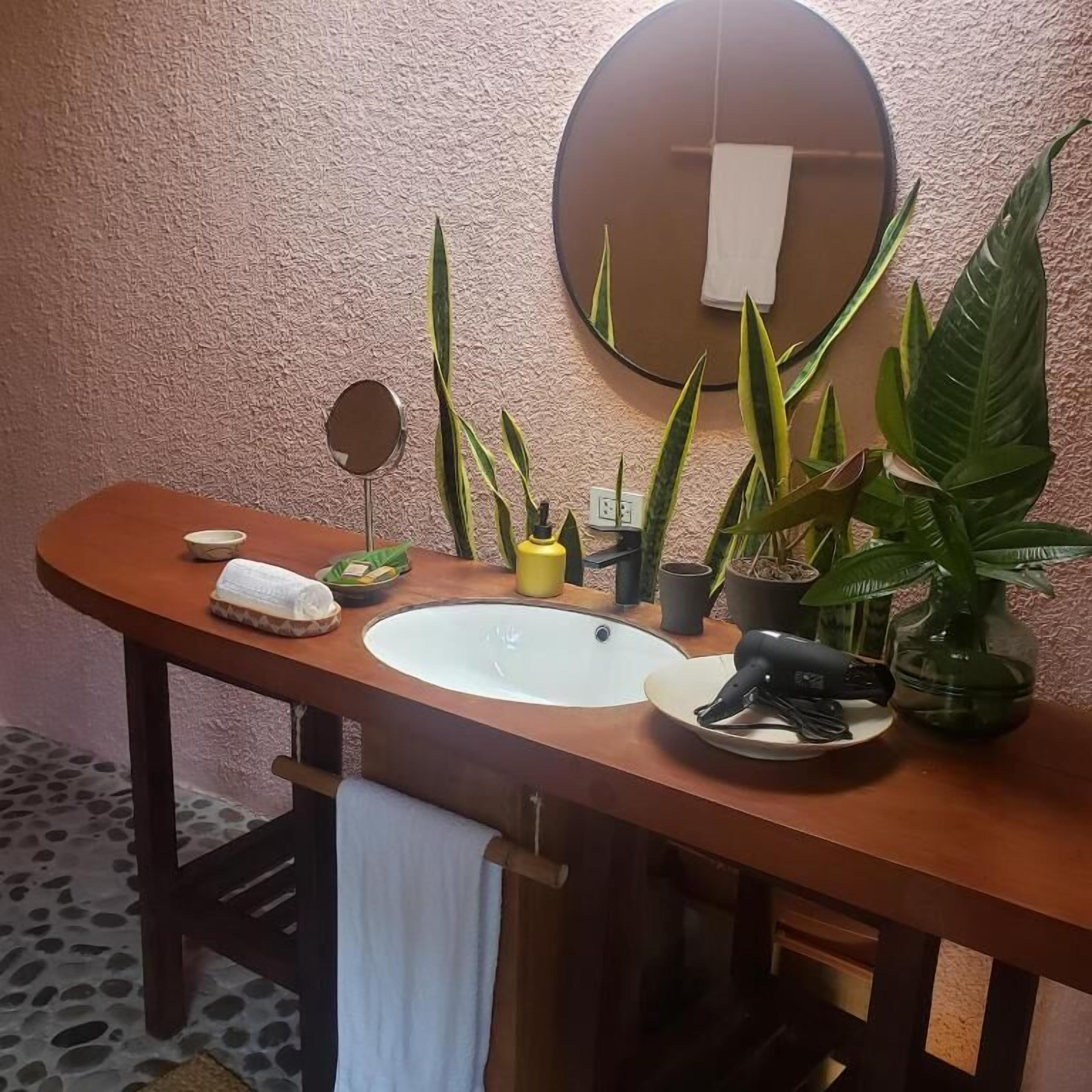 Un baño con un tocador de madera, un espejo redondo, un lavamanos y varias plantas en macetas.