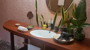 Un baño con un tocador de madera, un espejo redondo, un lavamanos y varias plantas en macetas.